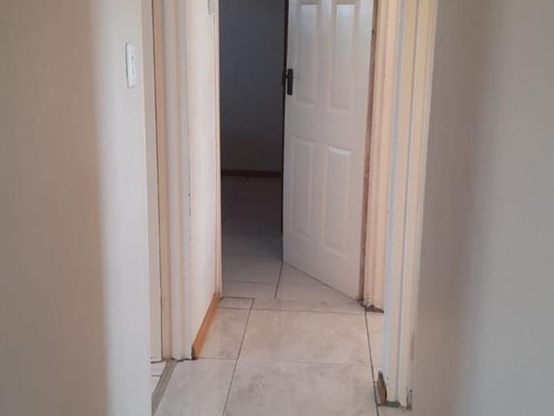 A narrow residential hallway featuring light-colored floor tiles and multiple internal doors, currently showing signs of wear and unfinished trim work.