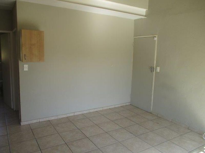 An empty living area featuring neutral tiled flooring and a wall-mounted storage cabinet, providing a blank canvas for interior design.