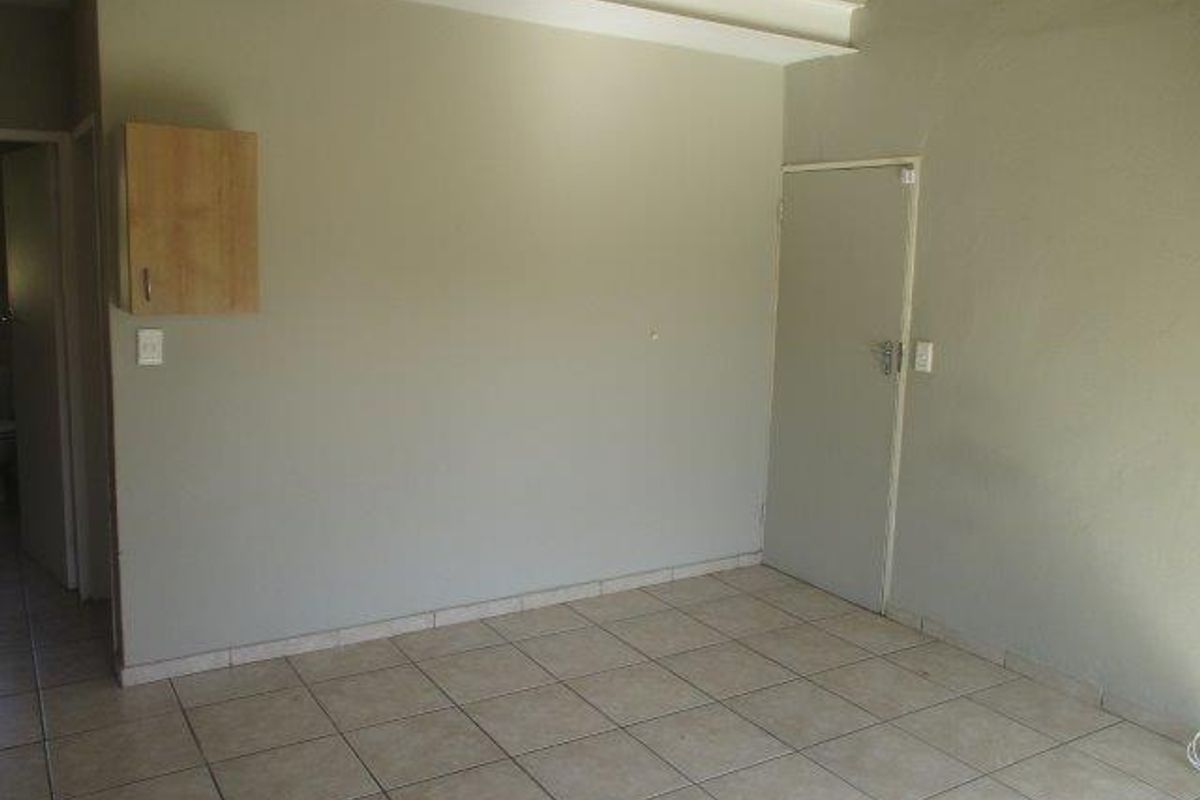 An empty living area featuring neutral tiled flooring and a wall-mounted storage cabinet, providing a blank canvas for interior design.