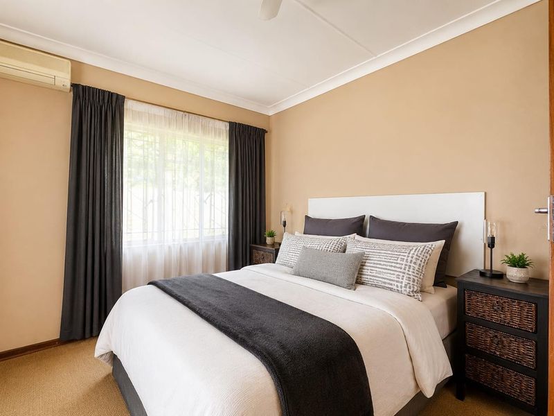A well-maintained bedroom featuring neutral wall tones, carpeted flooring, a ceiling fan, and a wall-mounted split-system air conditioning unit.