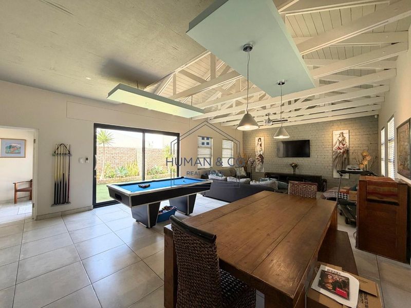 Spacious open-plan living area featuring exposed timber roof trusses, tiled flooring, and large sliding doors providing seamless access to the outdoor garden space.