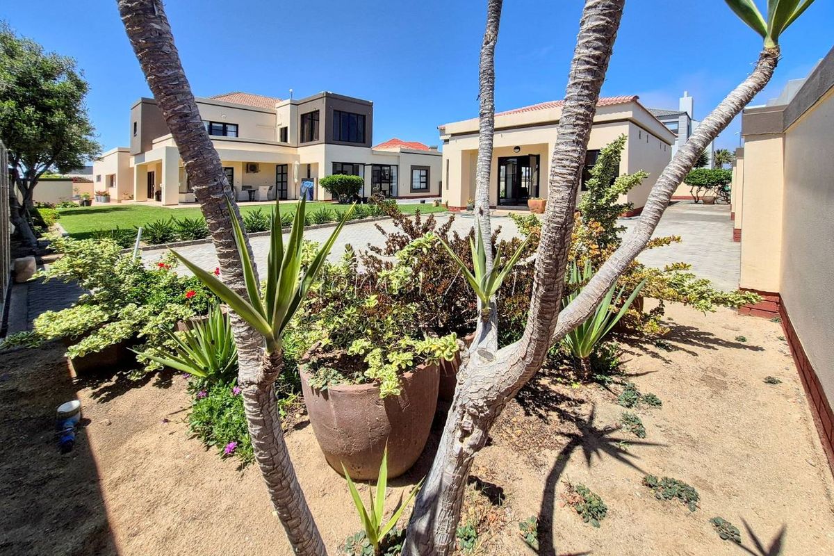 A spacious rear exterior view featuring a well-maintained paved driveway, landscaped garden areas, and modern multi-level residential structures under a clear blue sky.
