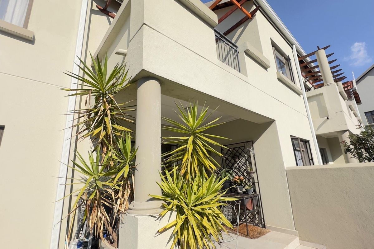 A view of the apartment exterior featuring a covered patio area, structural columns, and upper-level balcony with timber pergola detailing.