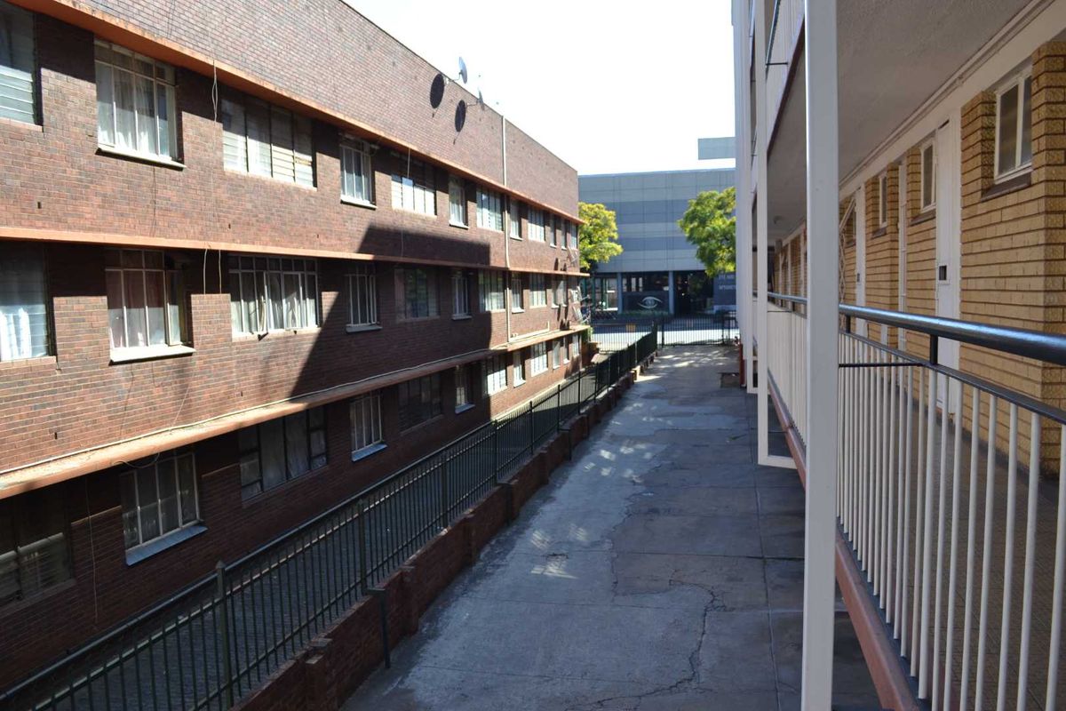 Exterior view of an apartment complex walkway featuring brick facade buildings, metal railings, and concrete flooring.