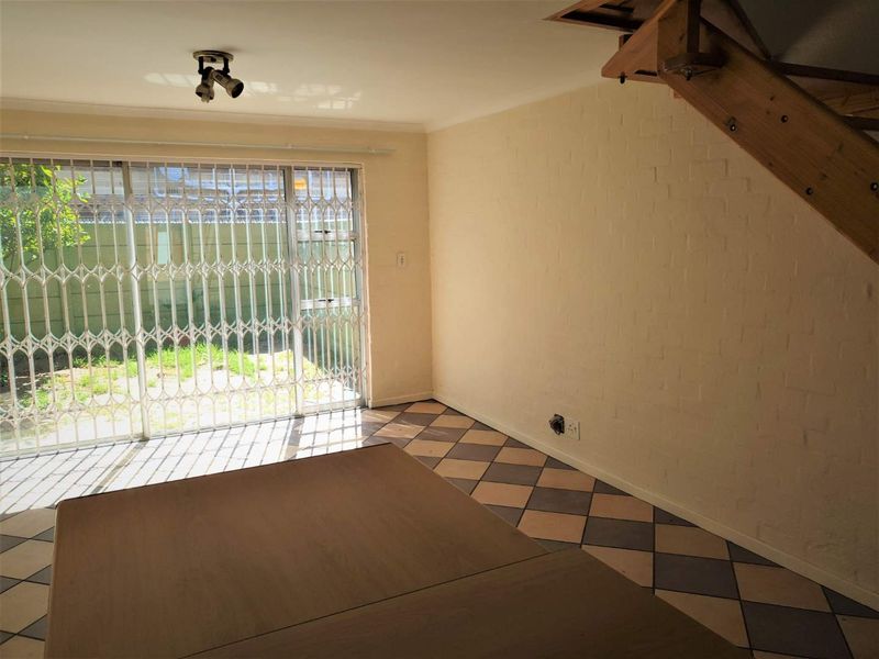 An empty living area featuring tiled flooring, a staircase, and a sliding glass door with a security gate leading to the garden.