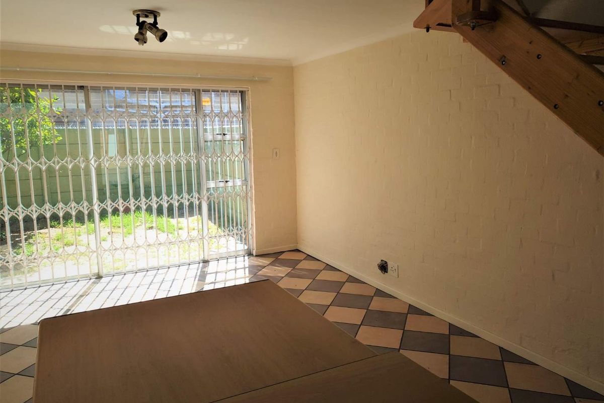 An empty living area featuring tiled flooring, a staircase, and a sliding glass door with a security gate leading to the garden.