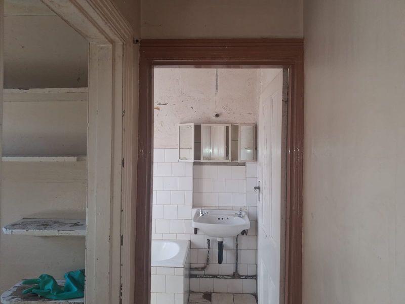 A dated bathroom requiring renovation, featuring a wall-mounted basin, built-in bathtub, and tiled splashback, with visible wear to wall and floor finishes.