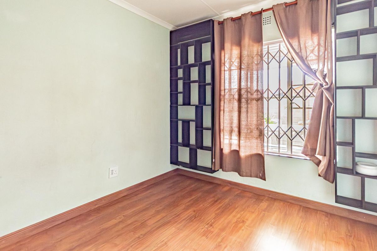 A bedroom featuring laminate flooring, built-in shelving units, and a window secured with metal burglar bars.
