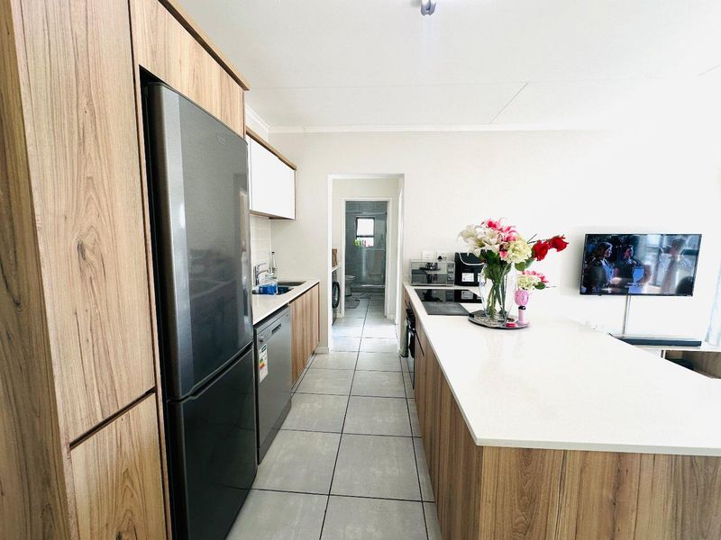 Modern kitchen featuring wood-finish cabinetry, stone countertops, a central island, and tiled flooring, with a clear view through to the adjacent bathroom area.