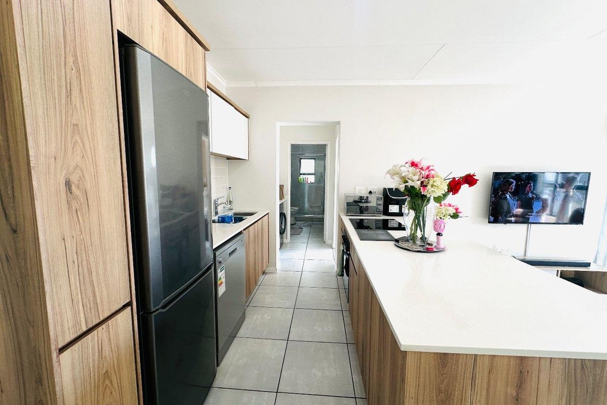 Modern kitchen featuring wood-finish cabinetry, stone countertops, a central island, and tiled flooring, with a clear view through to the adjacent bathroom area.