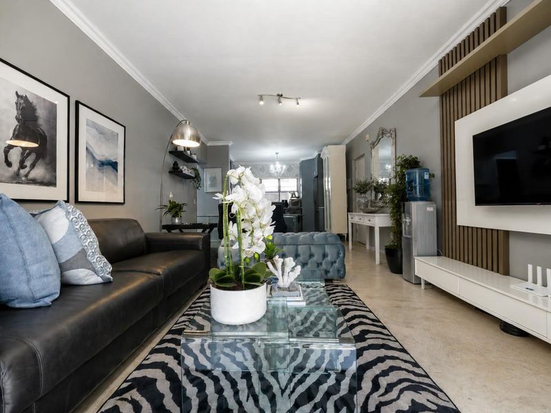 Spacious open-plan living area featuring a modern media wall with timber slat detailing, neutral tiled flooring, and elegant coving throughout.