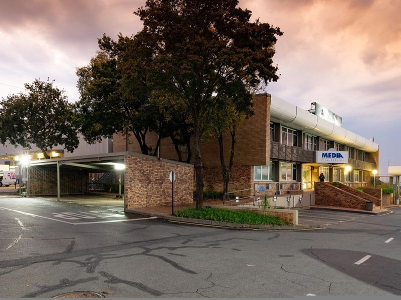 Front exterior view of an industrial property featuring a brick facade, covered parking area, and paved driveway with ramp access.