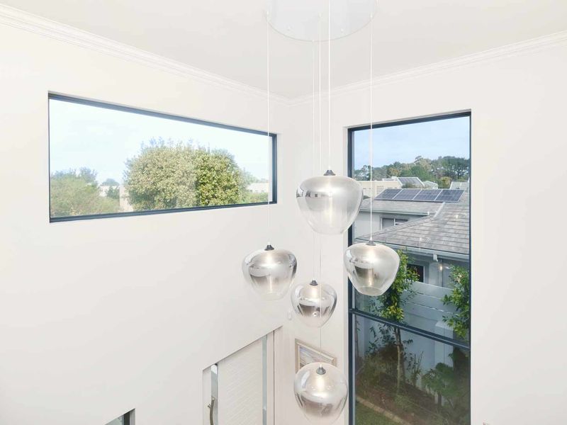 A bright, double-height entrance foyer featuring large windows that provide ample natural light and modern pendant lighting.