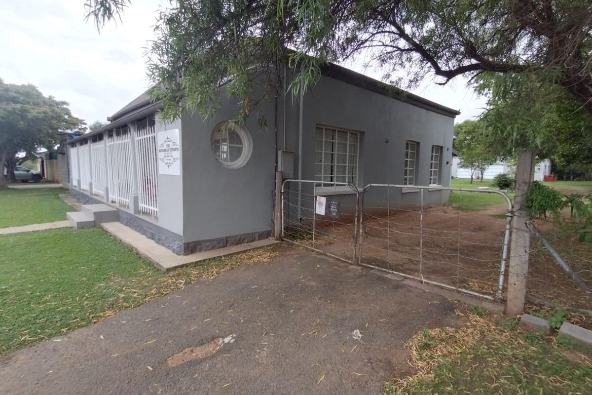 Exterior view of the property featuring a grey facade, circular window, metal security fencing, and a gated driveway entrance.