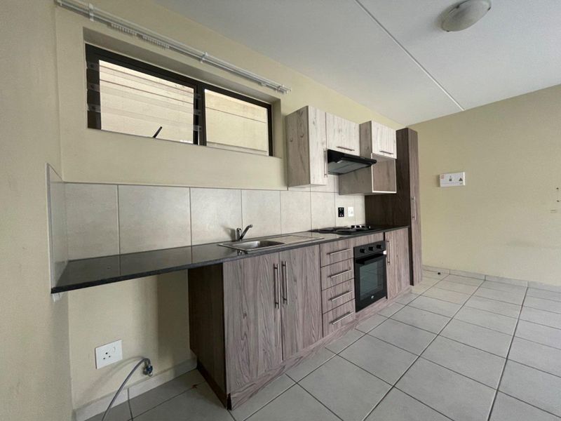 A clean, modern kitchen featuring wood-grain cabinetry, dark countertops, built-in oven and hob, and neutral tiled flooring.