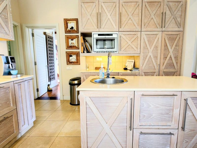 A functional kitchen featuring light wood cabinetry with cross-brace detailing, stone benchtops, an integrated microwave, and tiled flooring.