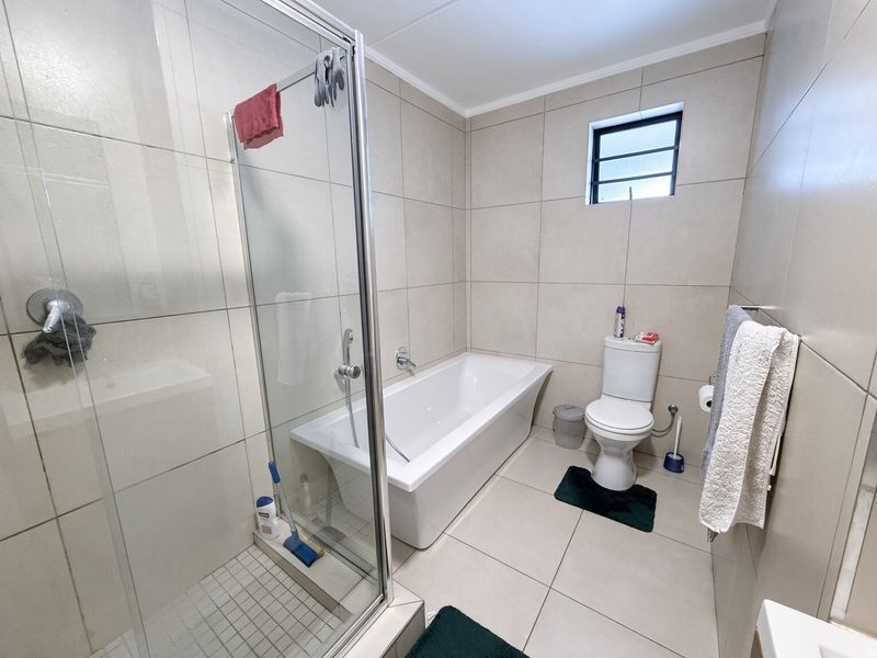 Modern bathroom featuring a glass-enclosed shower, a separate bathtub, and neutral ceramic tiling throughout.