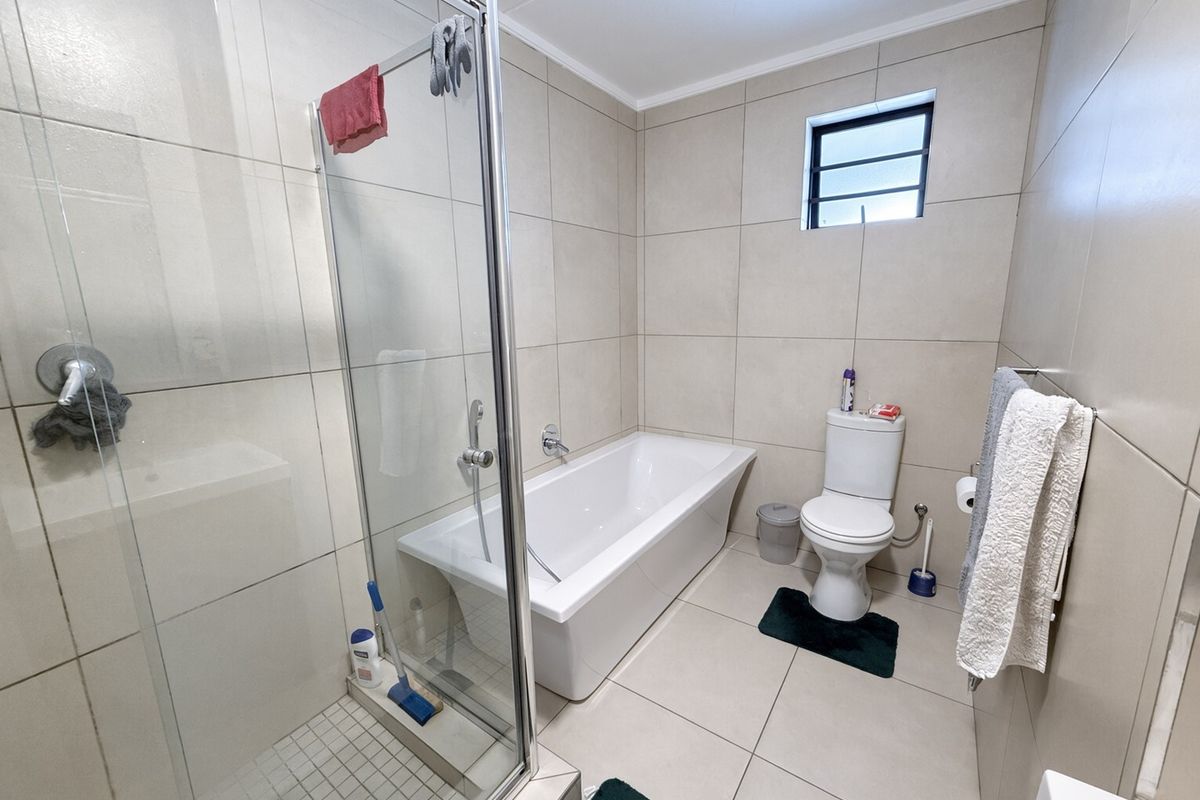 Modern bathroom featuring a glass-enclosed shower, a separate bathtub, and neutral ceramic tiling throughout.