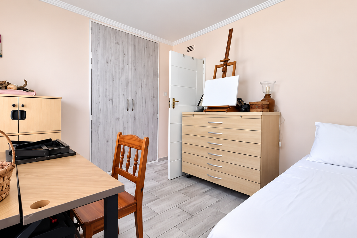 A well-maintained bedroom featuring light-toned laminate flooring, neutral walls, and a built-in wardrobe with wood-grain finish doors.