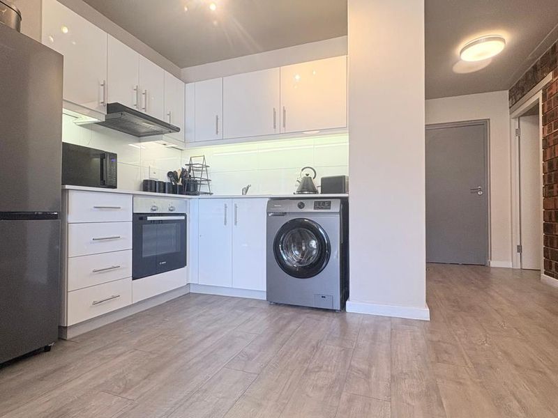 Modern kitchen featuring white cabinetry, integrated oven, extractor fan, and a stylish exposed brick feature wall, complemented by durable laminate flooring.