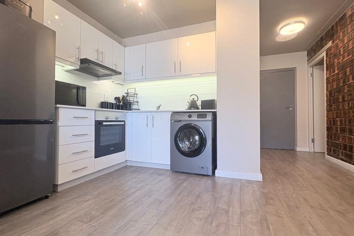 Modern kitchen featuring white cabinetry, integrated oven, extractor fan, and a stylish exposed brick feature wall, complemented by durable laminate flooring.