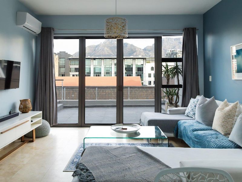 A bright living room featuring tiled flooring, a wall-mounted air conditioner, and large sliding doors opening onto a balcony with mountain views.