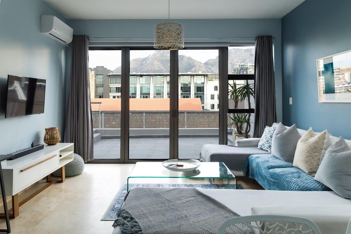 A bright living room featuring tiled flooring, a wall-mounted air conditioner, and large sliding doors opening onto a balcony with mountain views.