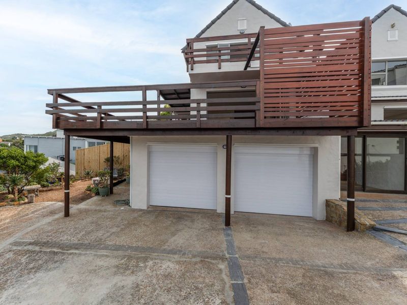 Front elevation featuring a double garage with white sectional doors and a large raised timber deck with privacy screening above.