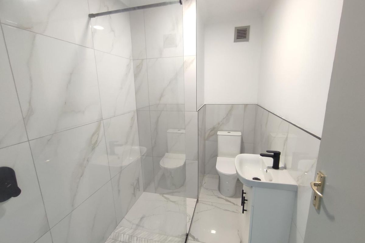 Modern bathroom featuring marble-look wall and floor tiles, a glass-enclosed walk-in shower, a contemporary vanity with a black faucet, and a white toilet.