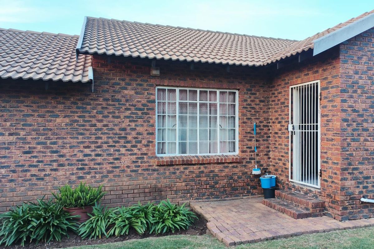 Exterior view of a face-brick house featuring a tiled roof, security gate, and a paved patio area adjacent to a small garden.