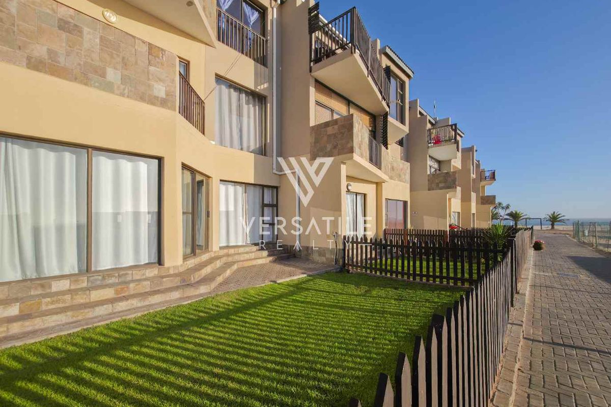 Rear view of a multi-story townhouse complex featuring private garden spaces, paved walkways, and balconies with metal railings.