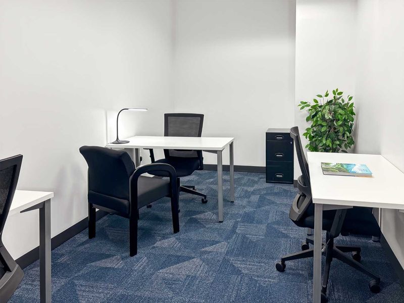 A clean and functional office space featuring blue patterned carpeting and neutral white walls, suitable for a professional work environment.