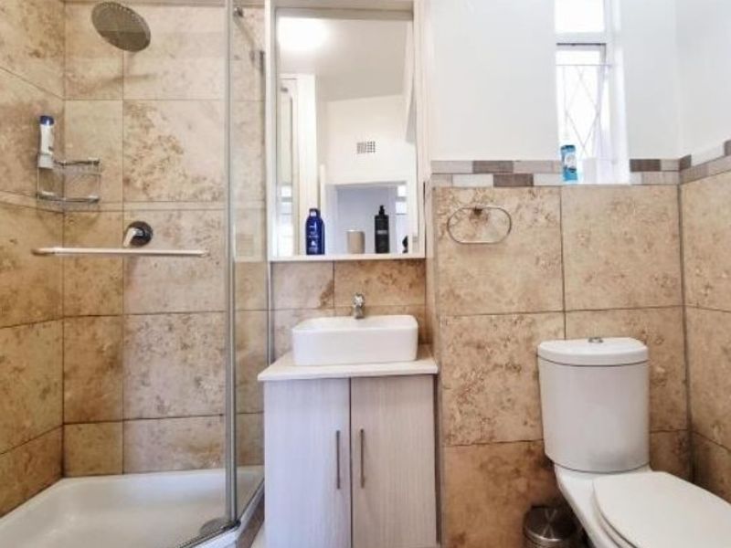 A well-maintained bathroom featuring a glass-enclosed shower, a modern vanity with a basin, and neutral stone-look wall tiling.