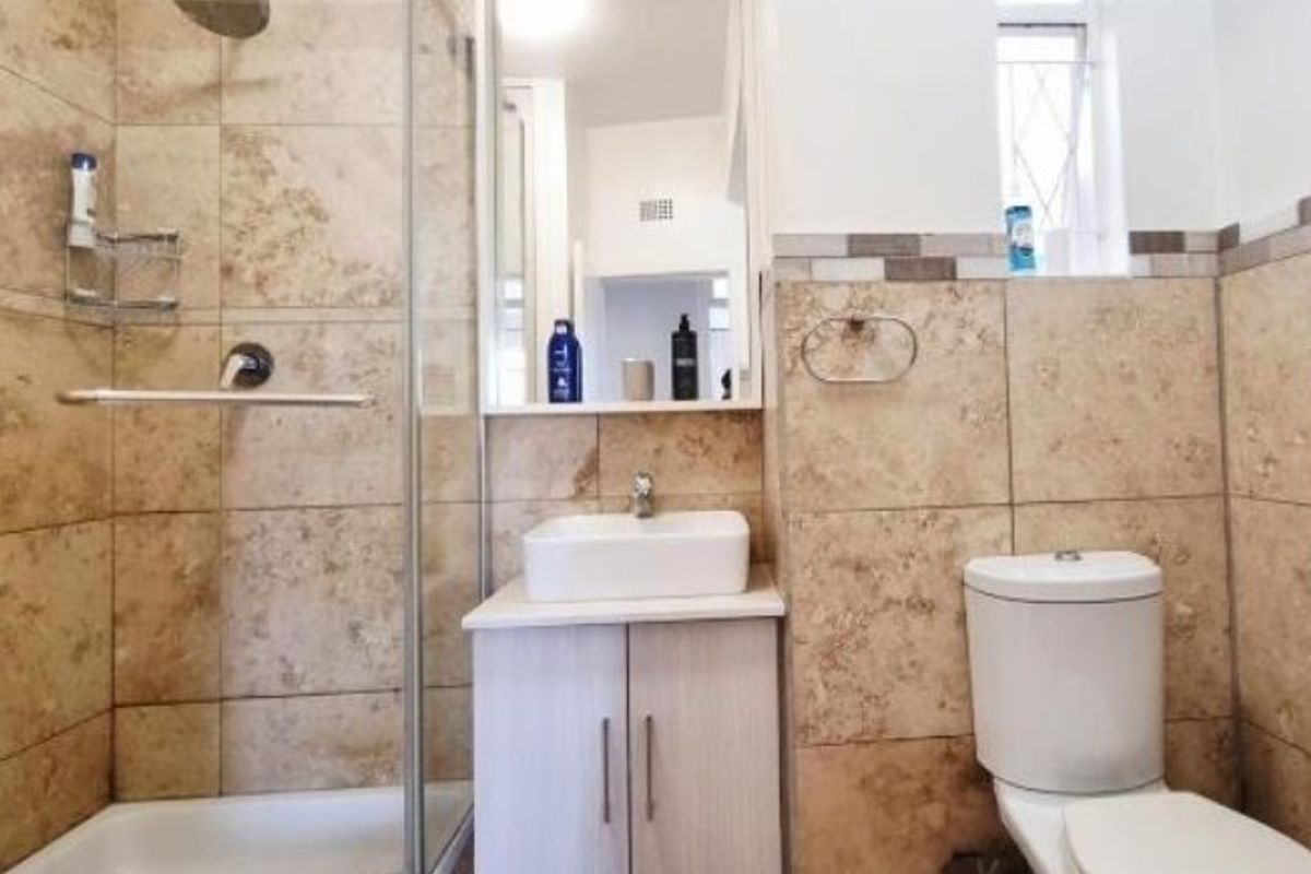 A well-maintained bathroom featuring a glass-enclosed shower, a modern vanity with a basin, and neutral stone-look wall tiling.