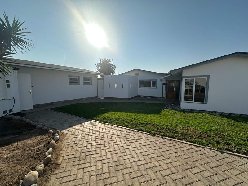 A well-maintained rear exterior view featuring a paved courtyard, manicured lawn, and clean white building facades with modern window frames.