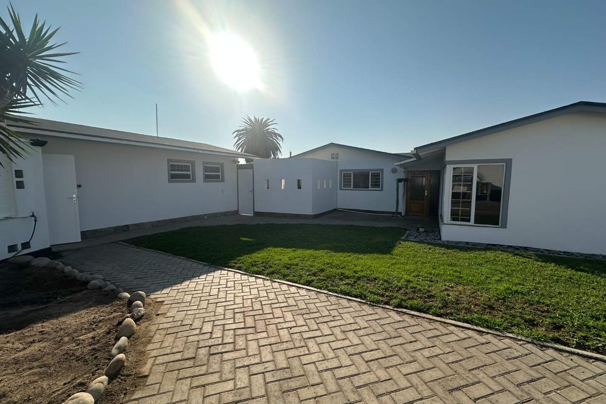 A well-maintained rear exterior view featuring a paved courtyard, manicured lawn, and clean white building facades with modern window frames.
