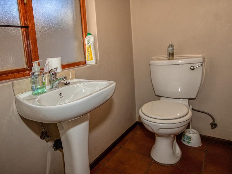 A compact bathroom featuring a pedestal basin, standard toilet, and tiled flooring with a timber-framed window.