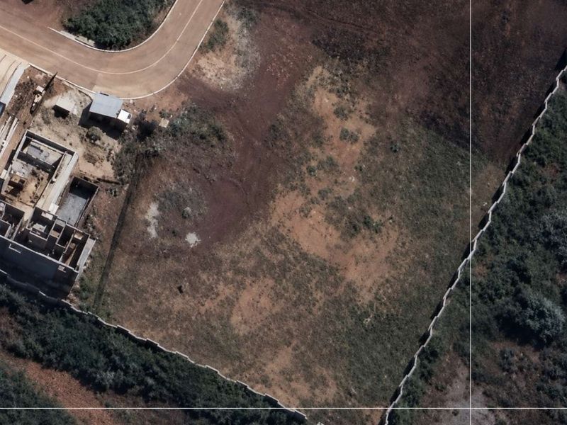 Aerial view of a vacant residential plot featuring perimeter walling and direct access to a paved road.