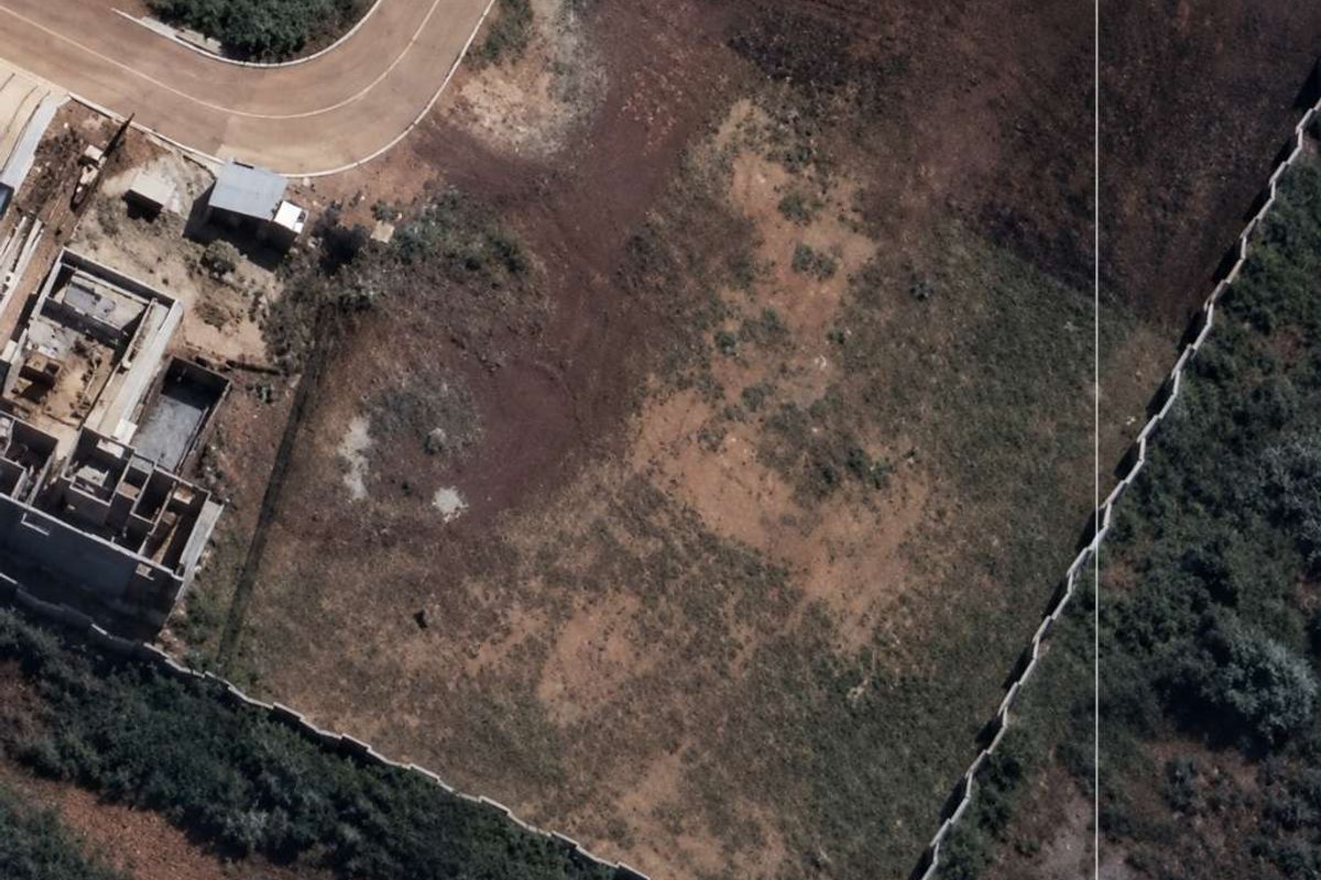 Aerial view of a vacant residential plot featuring perimeter walling and direct access to a paved road.