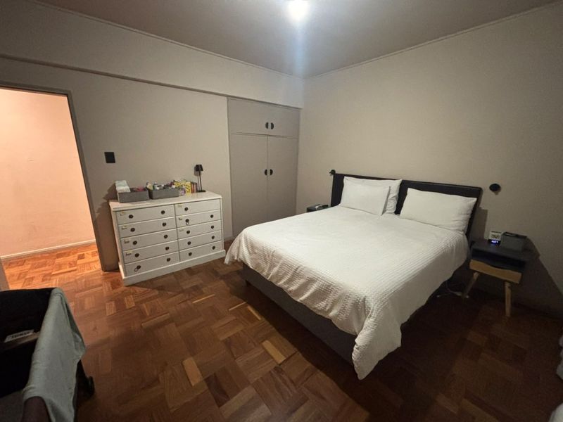 A bedroom featuring classic parquet flooring and a built-in wardrobe, offering a functional layout with neutral wall finishes.