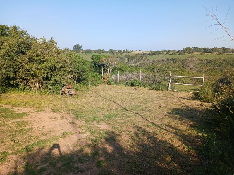 A view of a vacant residential plot featuring natural landscaping, perimeter wire fencing, and a wooden gate overlooking the surrounding rural landscape.