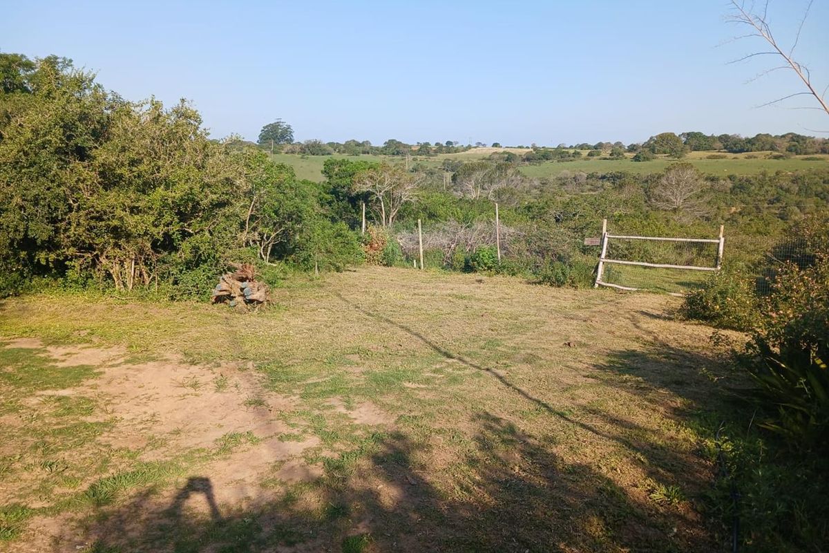 A view of a vacant residential plot featuring natural landscaping, perimeter wire fencing, and a wooden gate overlooking the surrounding rural landscape.