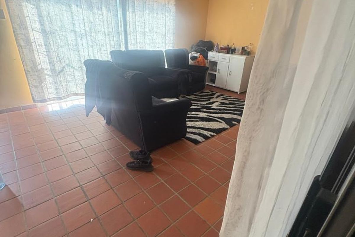 A living room featuring terracotta floor tiles and a large sliding glass door providing natural light, with walls requiring cosmetic attention.