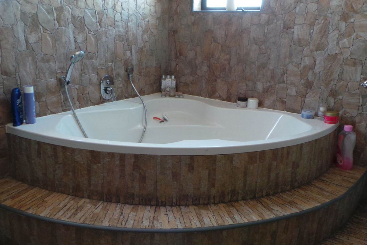A corner bathtub featuring stone-effect wall cladding and a raised tiled platform, providing a functional bathing area.