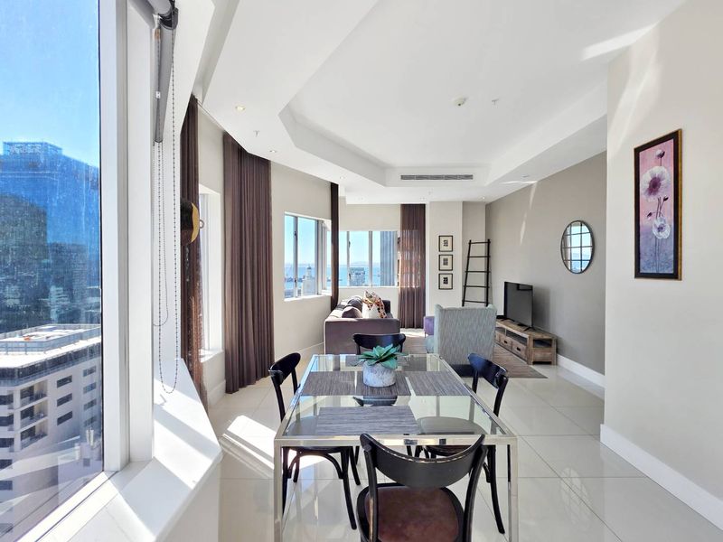 Bright open-plan living and dining area featuring tiled floors, recessed ceilings with ducted air conditioning, and expansive windows with city views.