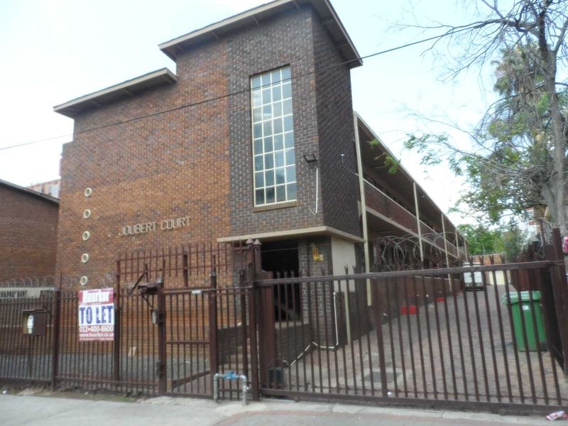 Exterior view of Joubert Court apartment building featuring a brick facade, secure metal gate, and paved driveway access.
