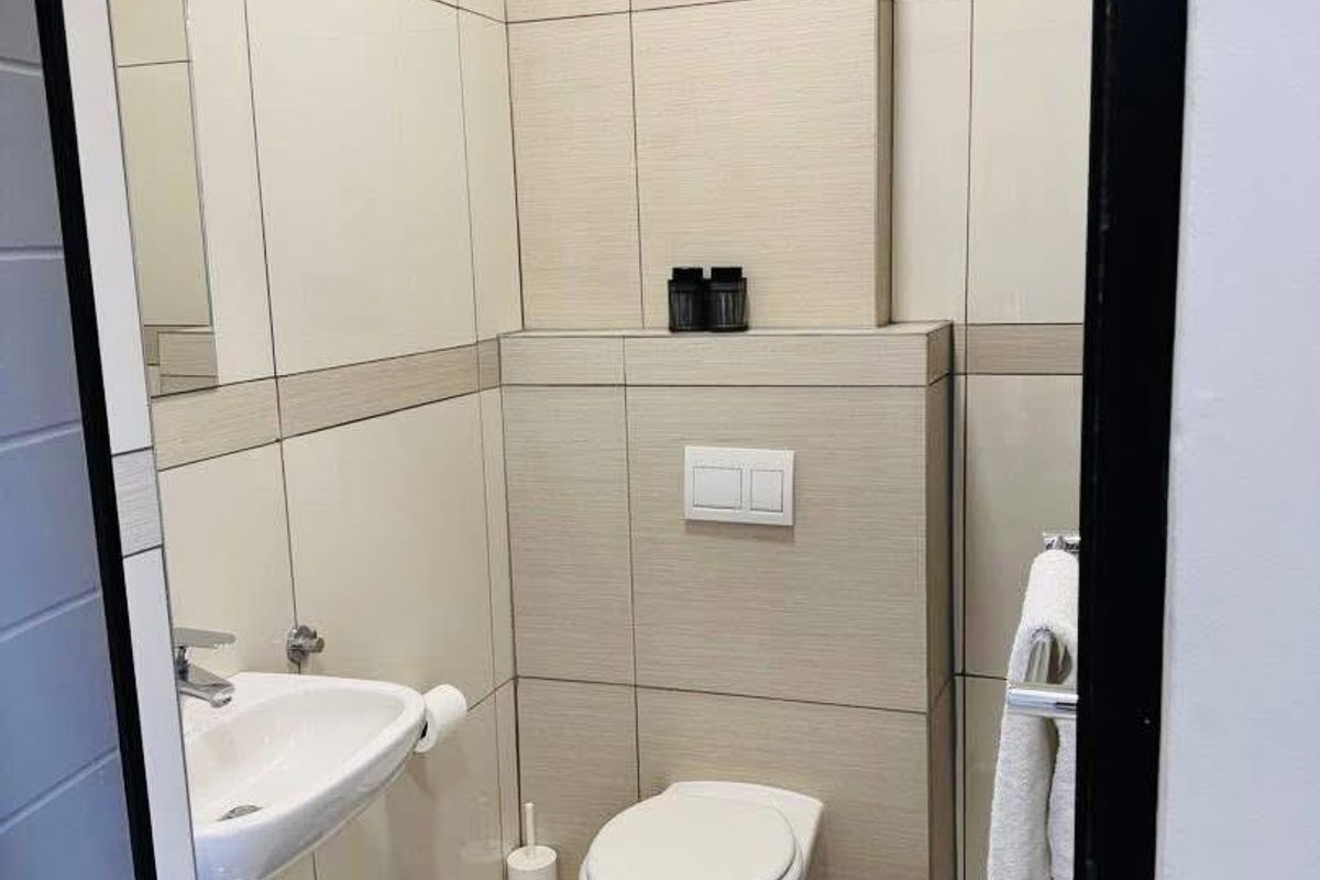 A modern, compact guest bathroom featuring neutral wall tiles, a wall-mounted toilet with a concealed cistern, and a sleek wall-hung basin.