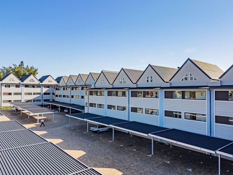 Aerial view of a modern apartment complex featuring multiple gabled rooflines, paved driveway, and extensive covered parking bays for residents.