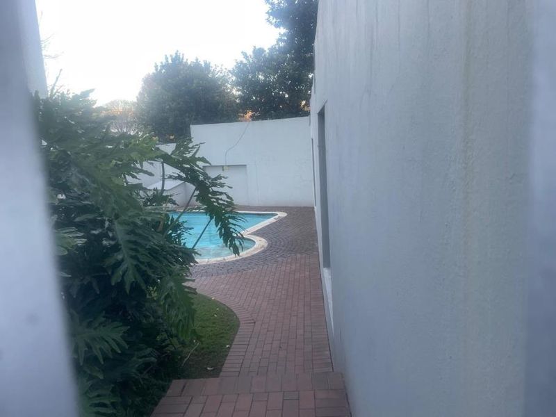 A view of a private swimming pool area with paved pathways and surrounding boundary walls, showing signs of weathering.