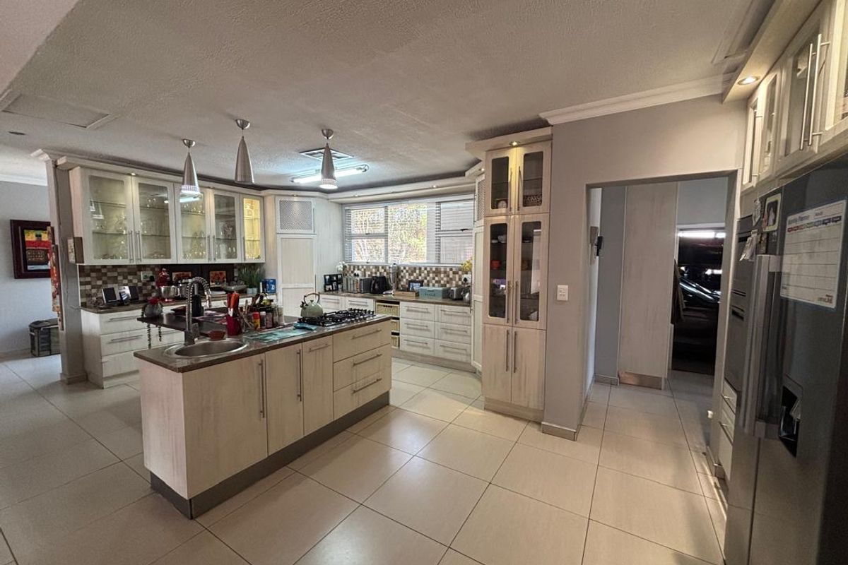 Spacious kitchen featuring a central island, ample built-in cabinetry, gas hob, integrated oven, and modern tiled flooring with neutral finishes.